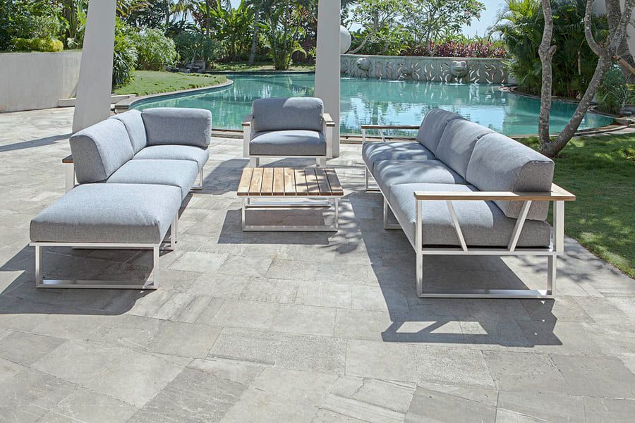 Ensemble de patio extérieur avec coussins gris, cadres blancs et table basse en bois près d'une piscine.