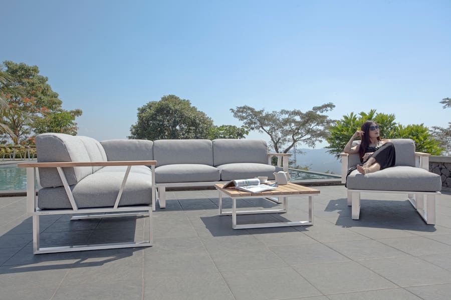 Ensemble de patio extérieur avec coussins gris, accents de bois et une personne se détendant.