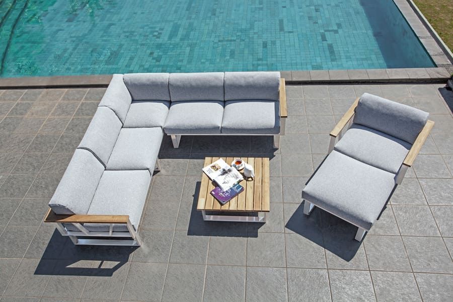 Canapé d'angle et fauteuil d'extérieur avec coussins gris et éléments en bois au bord d'une piscine.