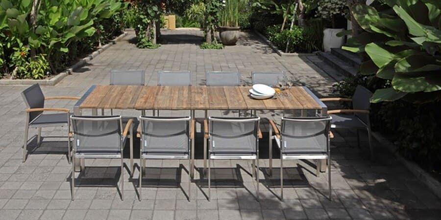 Table et chaises de jardin sur une terrasse pavée, entourée d'une végétation luxuriante.