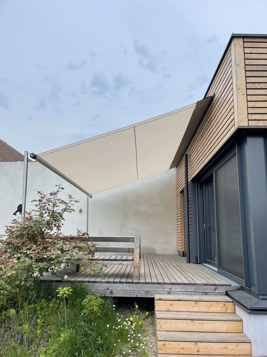 Une terrasse moderne en bois avec escalier et parasol blanc, jouxtant un bâtiment à bardage bois.