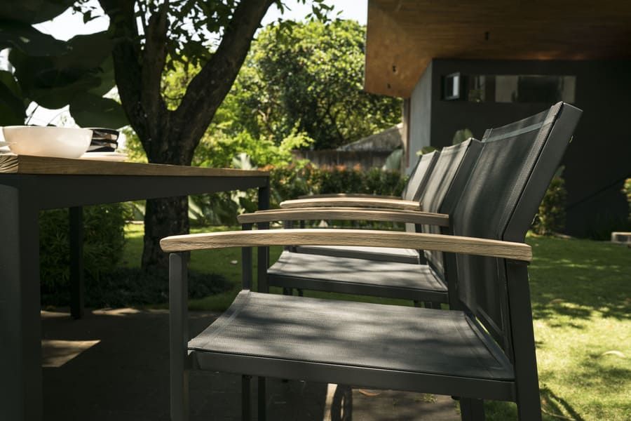 Ensemble de salle à manger d'extérieur avec chaises foncées et accoudoirs en bois sur une terrasse près d'un arbre.