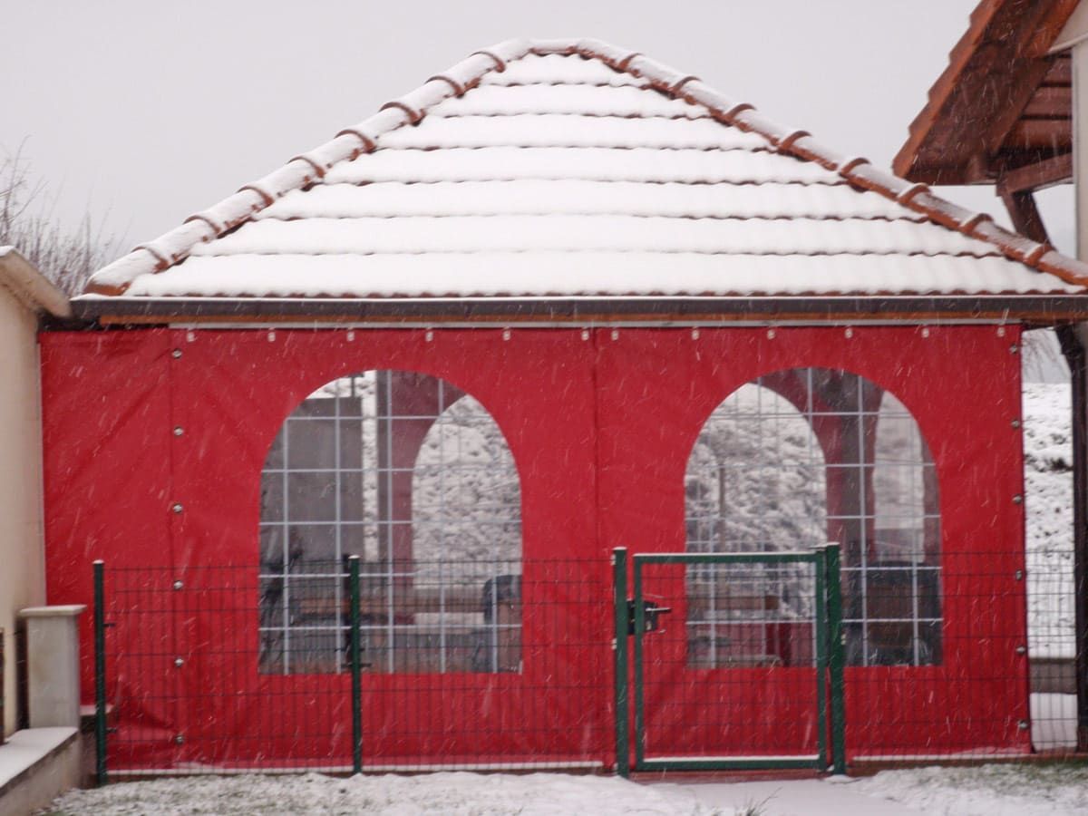Gazebo aux murs rouges et aux fenêtres cintrées sous un toit de tuiles blanches ; clôture verte.