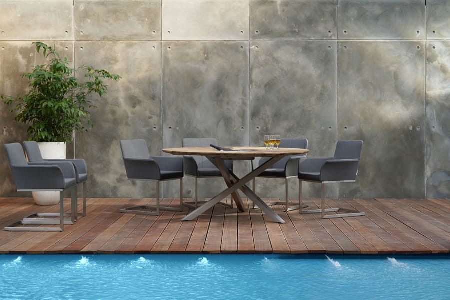 Ensemble de mobilier de jardin près d'une piscine. Table ronde en bois, chaises grises et mur en béton en arrière-plan.