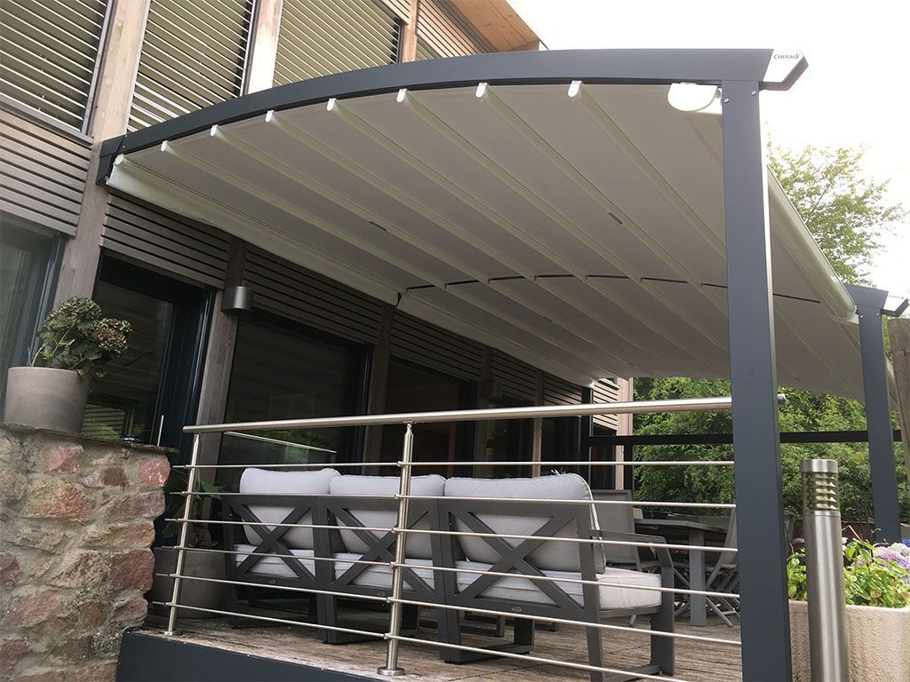 Une terrasse couverte avec du mobilier gris, un store rétractable et une rambarde en métal.