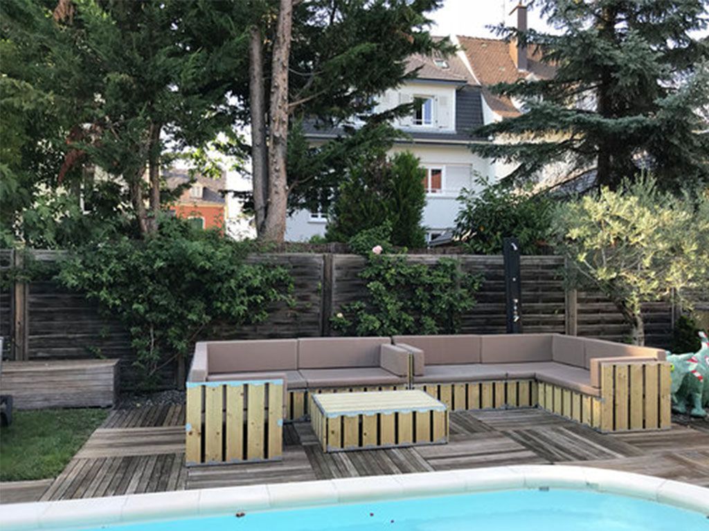 Canapé d'angle d'extérieur et table basse en bois, au bord d'une piscine.