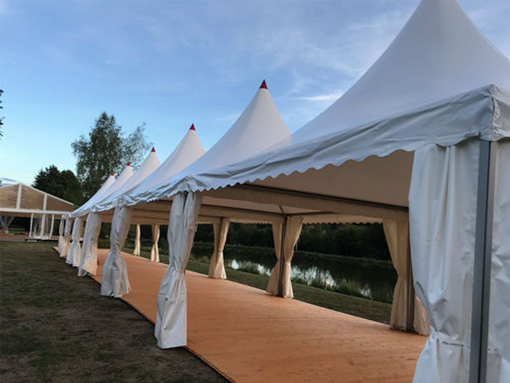 Des tentes blanches en forme de pagode étaient alignées le long d'une allée recouverte d'un tapis orange, près d'un point d'eau.