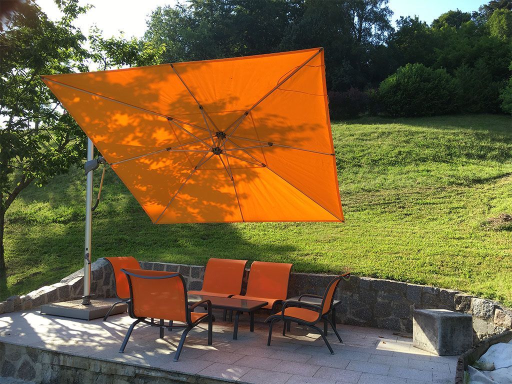 Parasol orange au-dessus d'un coin salon extérieur avec chaises et table par une journée ensoleillée.
