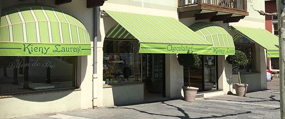Façade de magasin avec auvents à rayures vertes et blanches, enseigne du chocolatier Kieny Sauras.