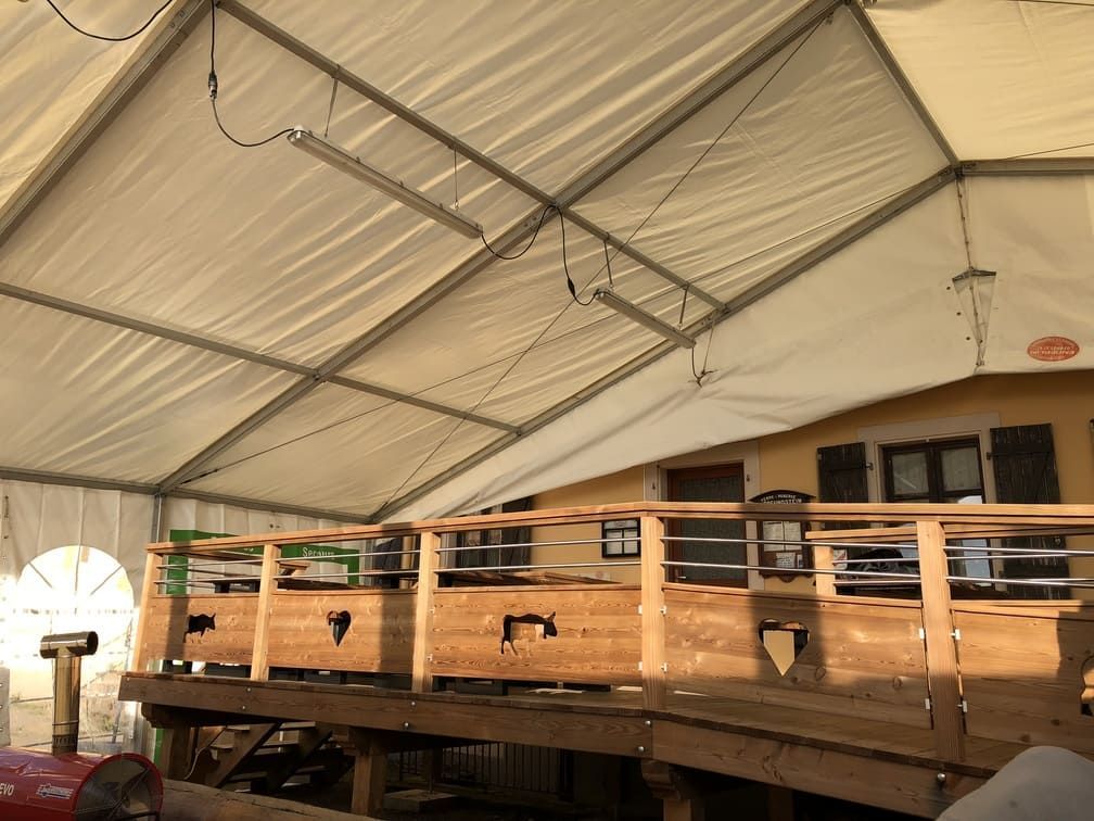 Terrasse en bois avec rambarde sous une grande tente. Bâtiment avec fenêtres visible derrière la terrasse.