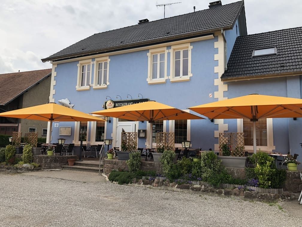 Un restaurant bleu clair avec des parasols orange et une terrasse.