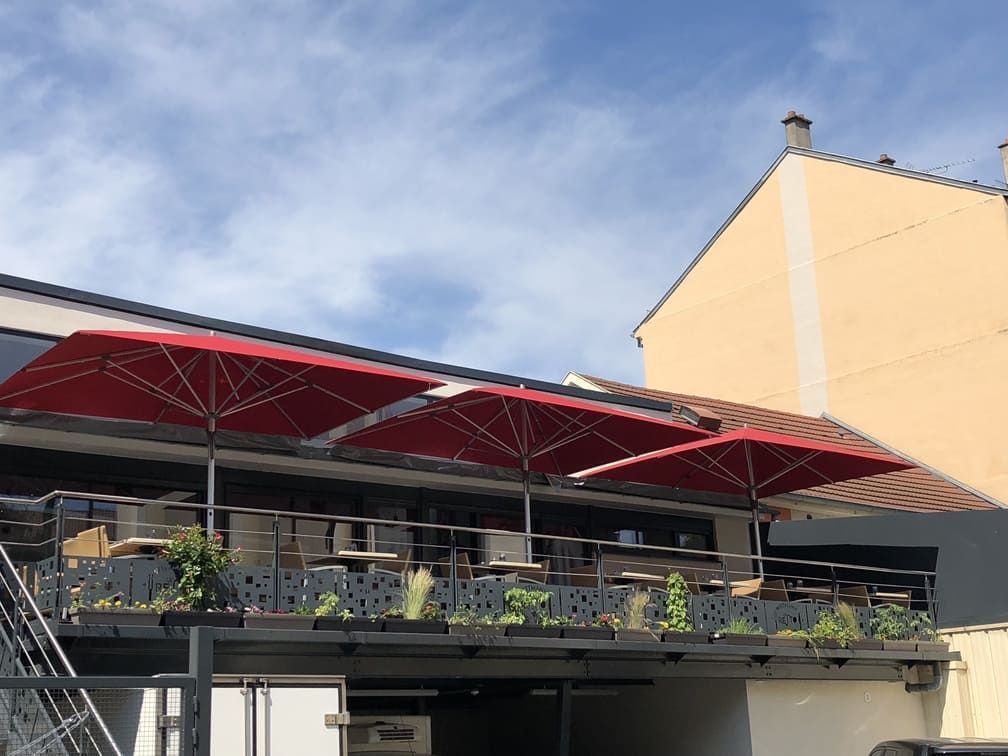 Terrasse extérieure de restaurant avec parasols rouges et tables sous un ciel bleu.