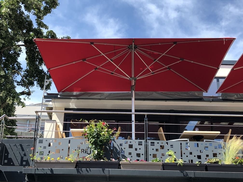 Parasol rectangulaire rouge au-dessus de la terrasse d'un restaurant avec une balustrade à motifs carrés.