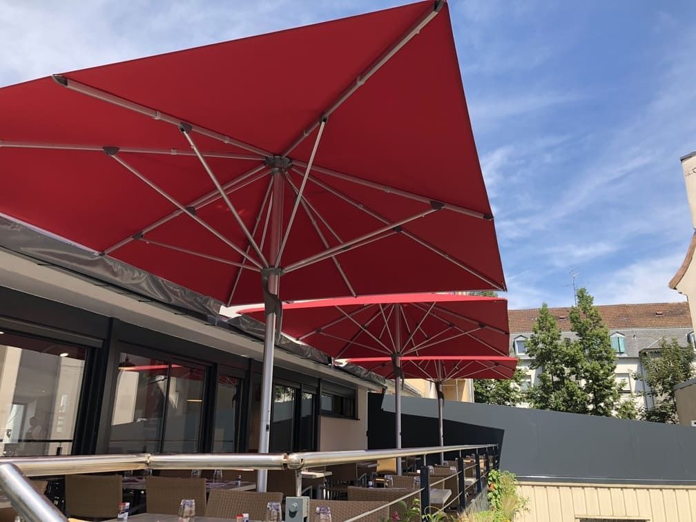 Parasols rouges d'extérieur au-dessus de la terrasse d'un restaurant, ciel bleu en arrière-plan.