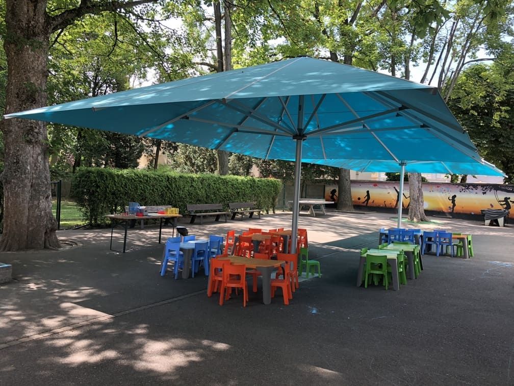 Espace extérieur avec tables et chaises colorées sous un grand parasol bleu.