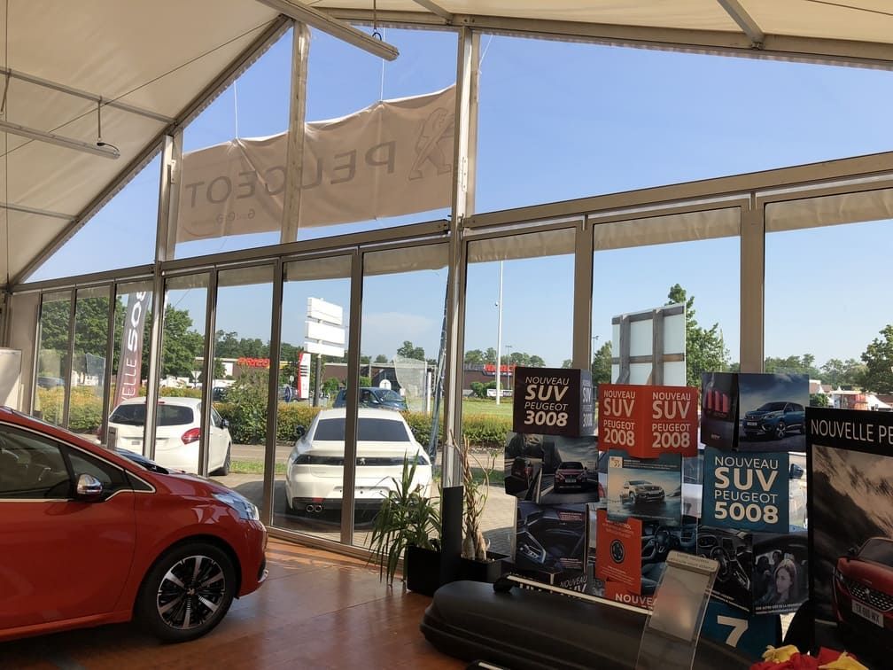 À l'intérieur d'une tente de concessionnaire Peugeot, on aperçoit des affiches orange de voitures et de SUV.