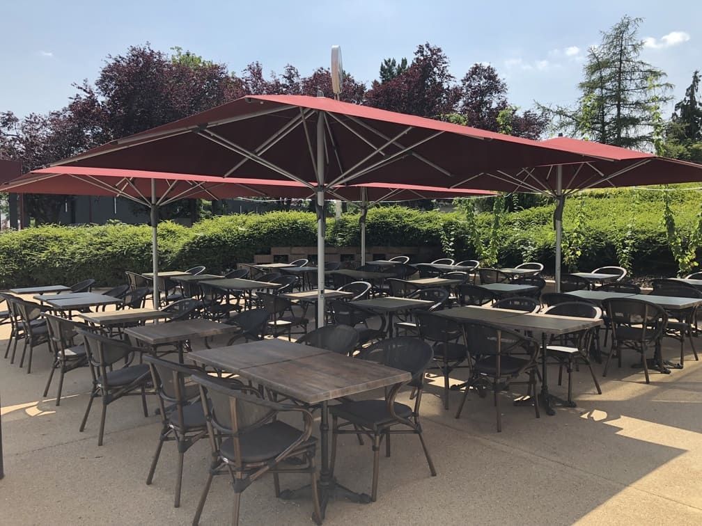 Espace repas extérieur avec tables et chaises sous de grands parasols rouges.