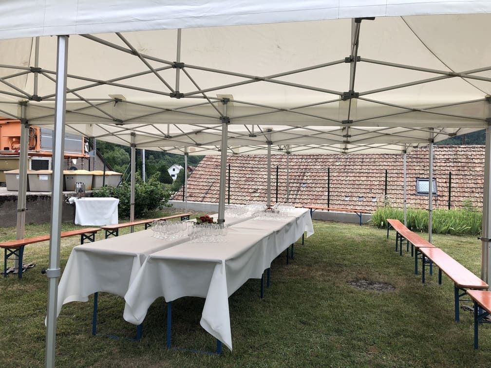 Une tente de réception installée sur une pelouse, avec de longues tables, des bancs et des verres.