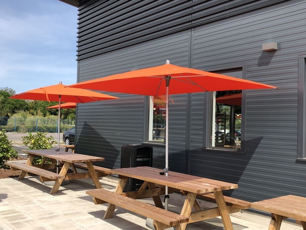 Tables de pique-nique avec parasols orange devant un bâtiment par une journée ensoleillée.
