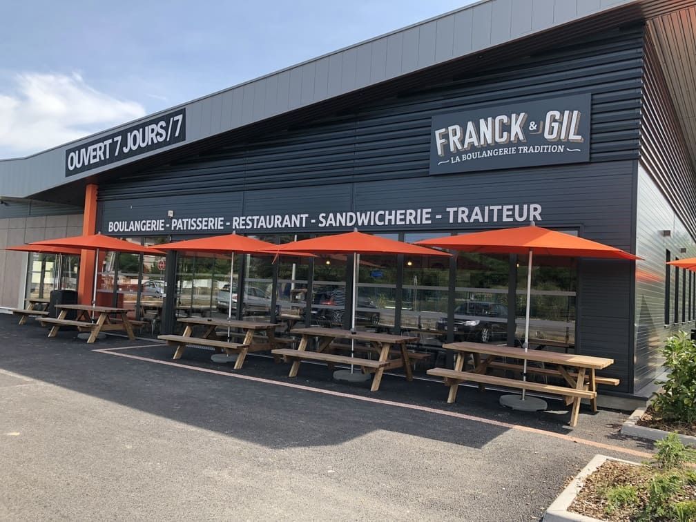 Extérieur de la boulangerie Franck Gil avec terrasse et parasols orange.