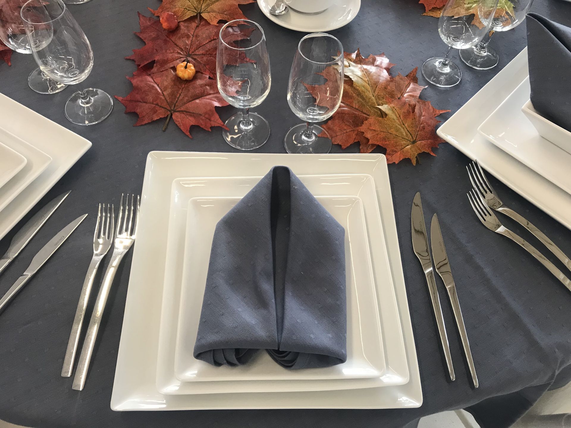 Dressage de table formel avec assiettes carrées blanches, couverts et serviette grise.
