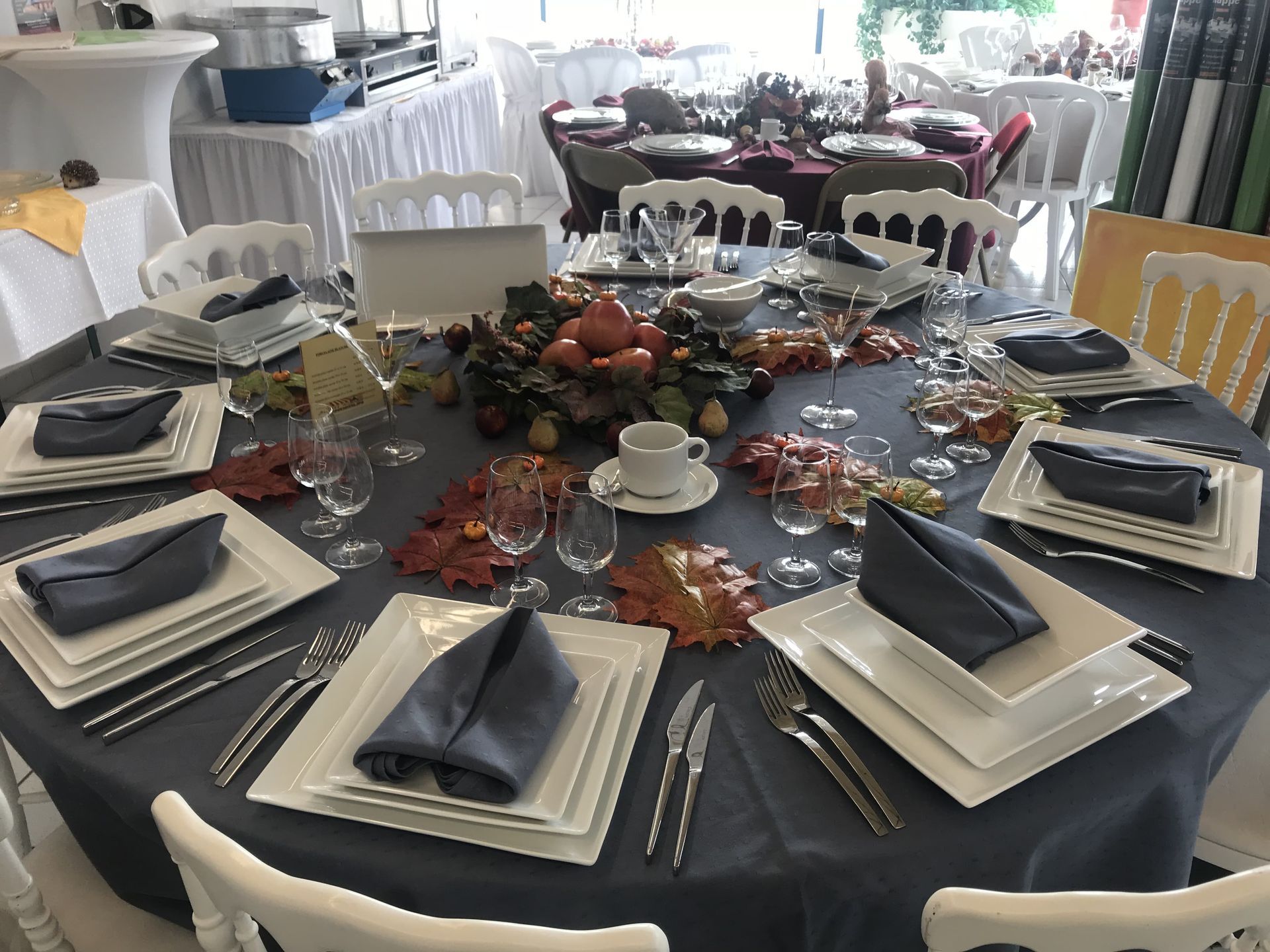 Élégante table dressée pour un événement formel, avec nappe grise, assiettes carrées blanches et centres de table automnaux.