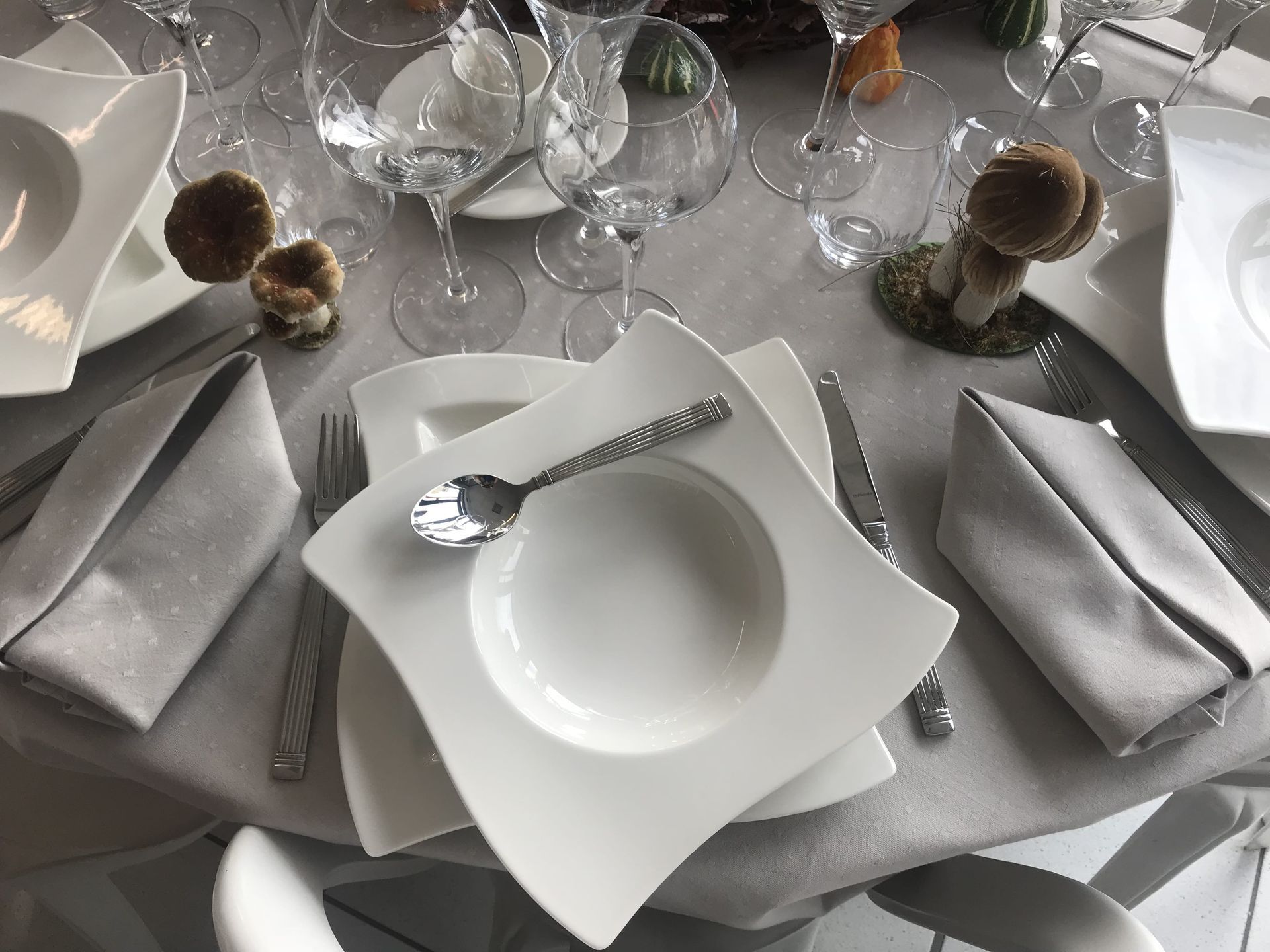 Une table élégamment dressée avec des assiettes carrées blanches, des couverts et des serviettes grises.