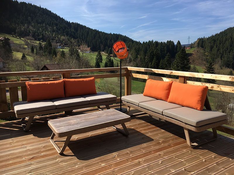 Terrasse en bois avec sièges et table basse, coussins orange, vue sur la montagne.