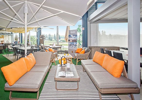 Aménagement de mobilier d'extérieur : chaises longues avec coussins orange, table basse, tapis rayé, parasols, vue sur le paysage extérieur.