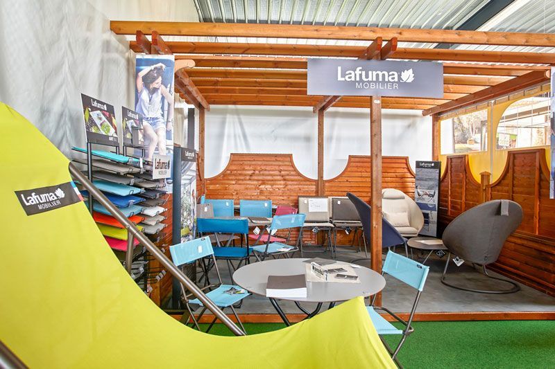 Un stand Lafuma Mobilier lors d'un salon professionnel, avec des chaises, une table et un tissu jaune dans une structure en bois.