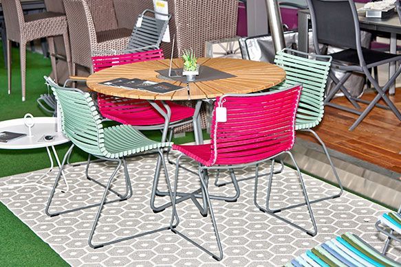 Table de patio ronde en bois avec quatre chaises ; deux vertes, deux rouges ; disposées sur un tapis.