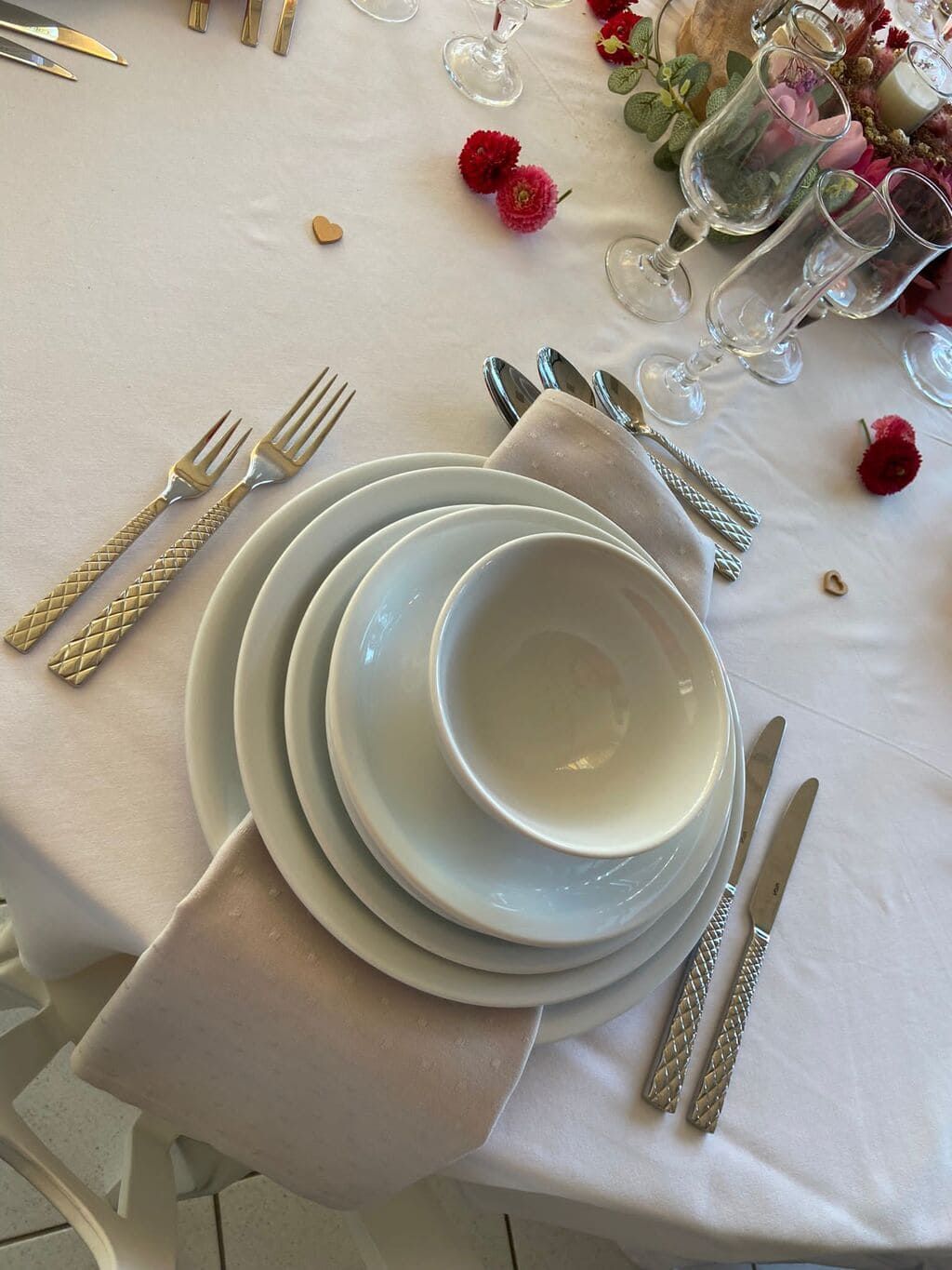 Dressage de table formel : assiettes blanches, bol, couverts, serviette rose, nappe et fleurs.