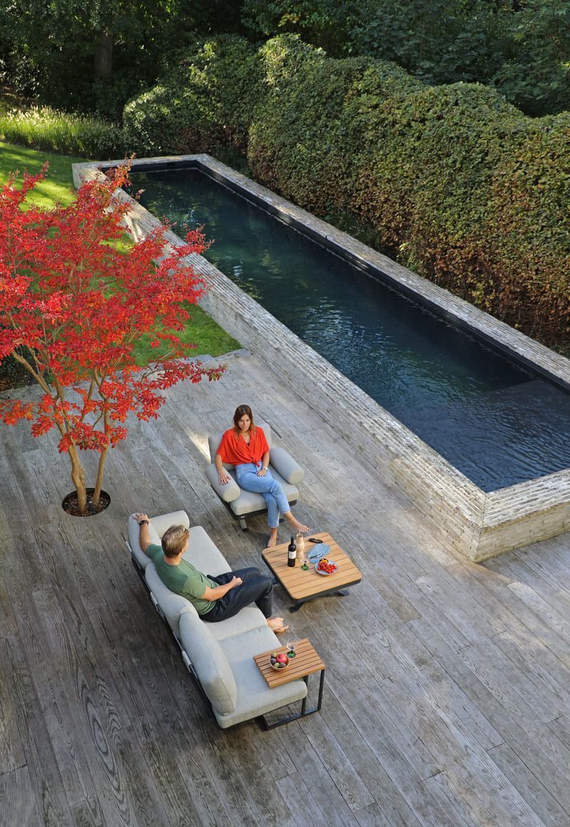 Deux personnes se détendent sur des chaises longues près d'une longue piscine dans un jardin. Érable rouge.
