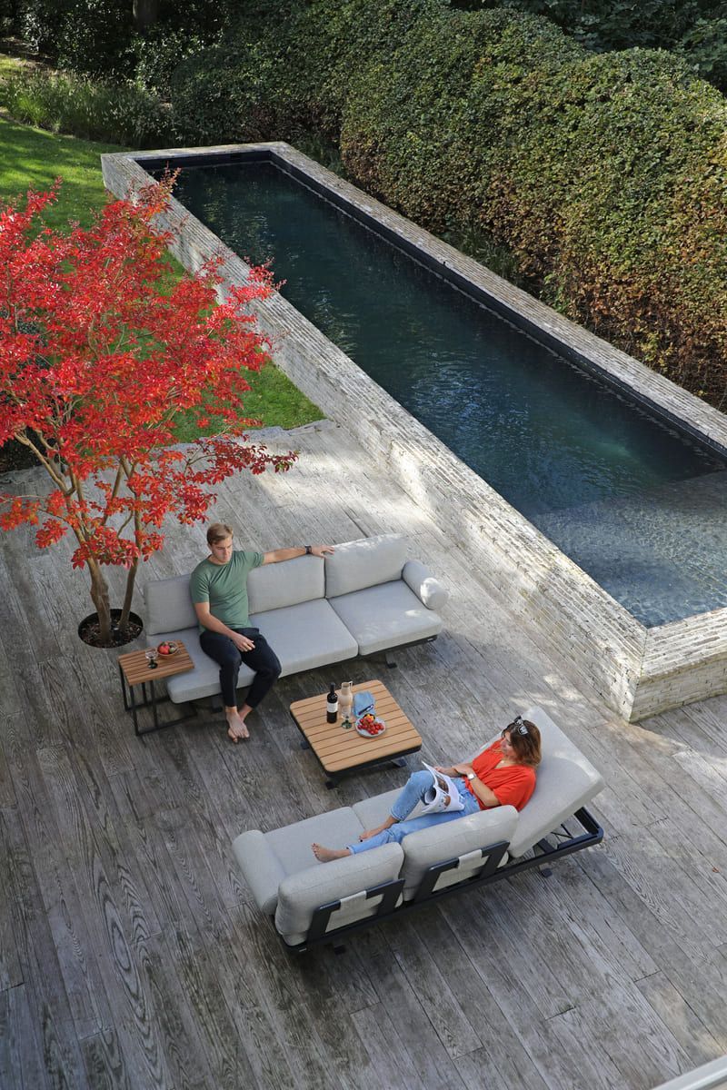 Un couple se détend près d'une longue piscine et de mobilier moderne sur une terrasse agrémentée d'un arbre rouge.