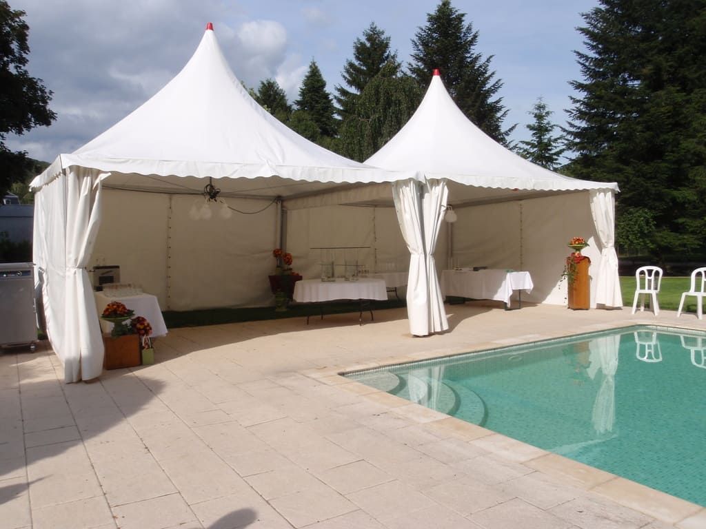 Une tente blanche pour événements au bord de la piscine, avec des tables et des fleurs à l'intérieur.