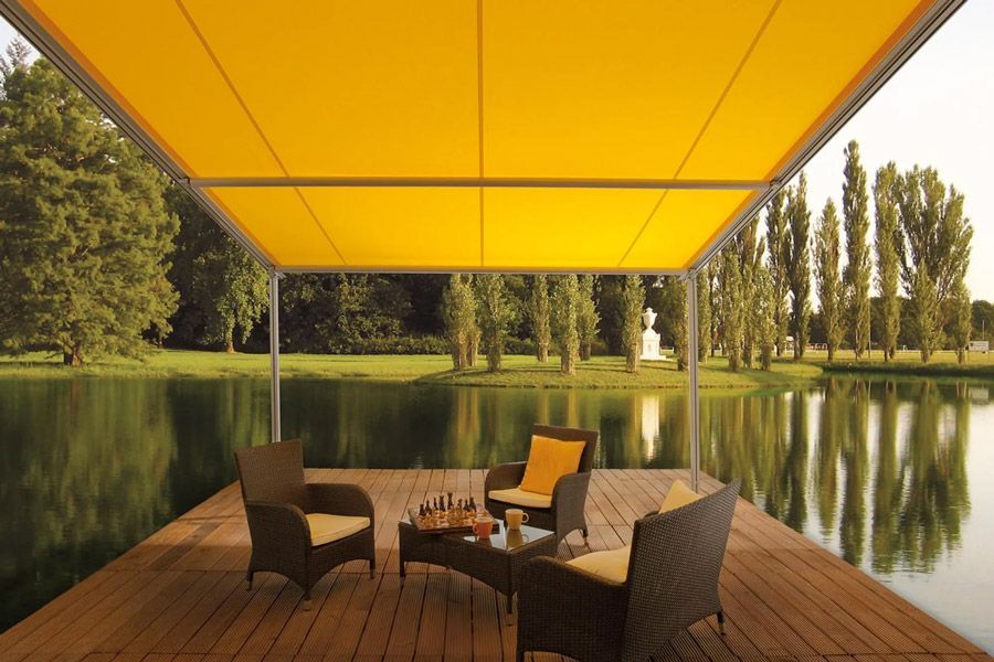 Auvent jaune au-dessus d'une terrasse au bord du lac, avec des chaises et une table.