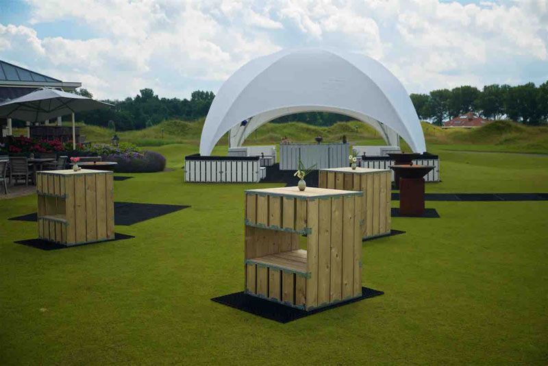 Aménagement d'un espace extérieur pour un événement, avec un auvent blanc, des tables en bois et de la pelouse verte.