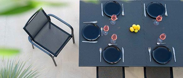 Vue aérienne d'une table dressée pour six personnes avec des assiettes noires, des couverts et des boissons, à côté d'une chaise.