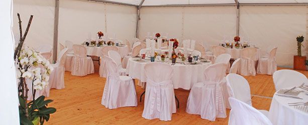 L'intérieur d'une tente décorée avec des tables rondes recouvertes de nappes blanches et des housses de chaises ; des fleurs sur les tables.