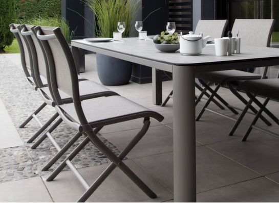 Table de jardin avec chaises installées sur une terrasse. La table est dressée avec de la vaisselle et des boissons.