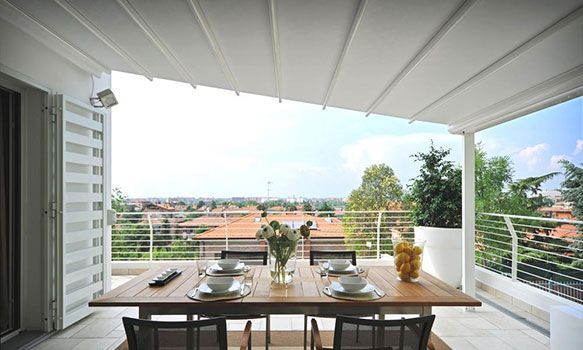 Terrasse aménagée avec une table dressée pour un repas, offrant une vue sur la ville. Store rétractable au-dessus.