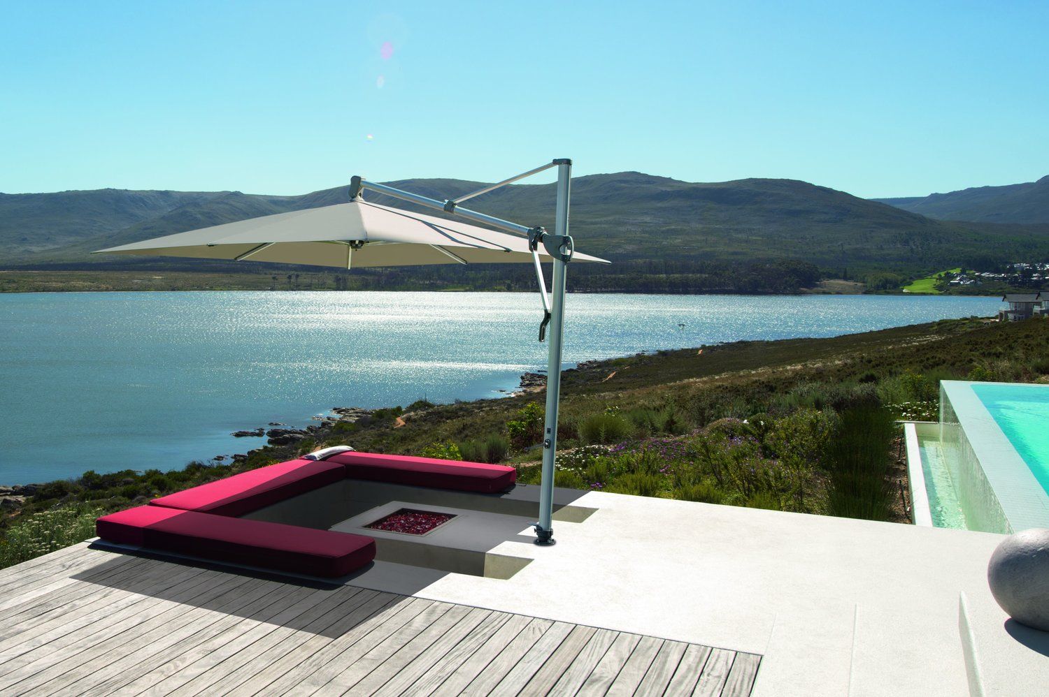 Terrasse extérieure avec canapé d'angle rouge, parasol et vue sur un lac et les montagnes.