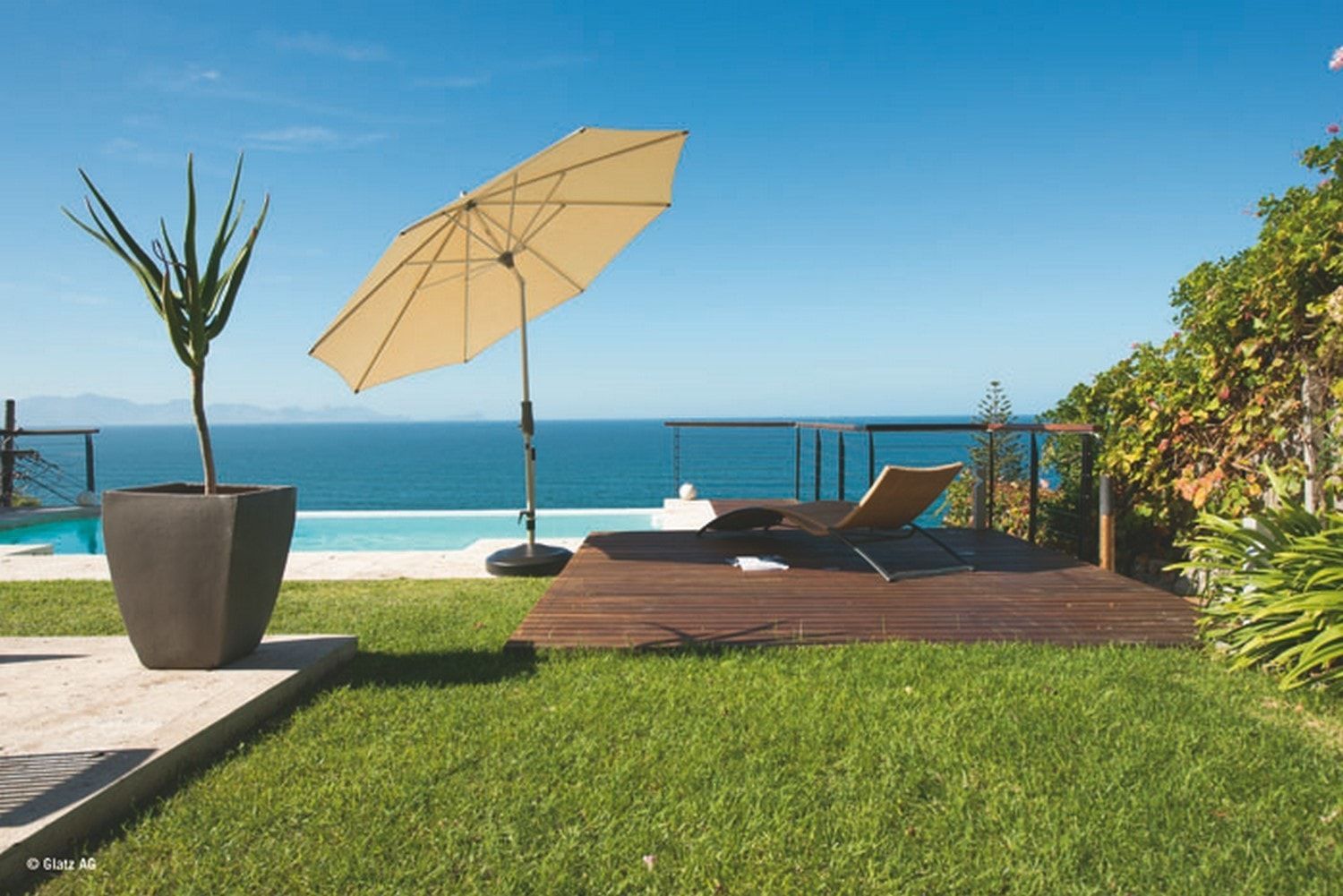 Chaise longue sous un parasol sur une terrasse en bois au bord d'une piscine avec vue sur l'océan.