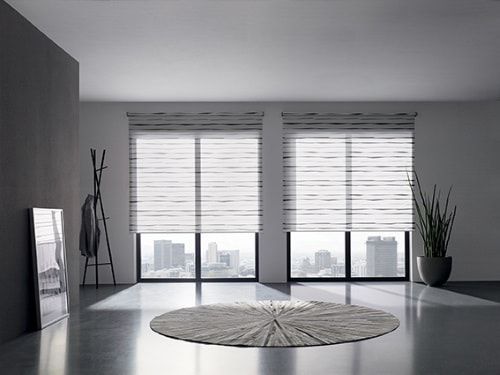 Chambre moderne avec vue sur la ville, deux fenêtres avec stores, porte-manteau, tapis et plante.