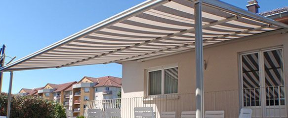 Une maison blanche avec un auvent rayé qui s'étend au-dessus d'un balcon, par une journée ensoleillée.