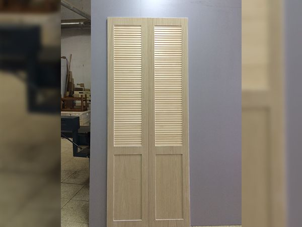 Par de puertas de armario con lamas de madera sin terminar, apoyadas contra una pared violeta sencilla.
