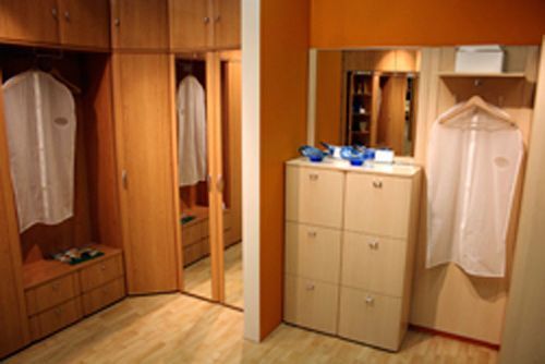 Un armario de madera con ropa colgada, incluyendo un espejo y un zapatero. Las paredes son naranjas y beige.