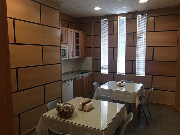 Una pequeña cocina y comedor con paneles de madera de color claro, dos mesas y un pequeño refrigerador.