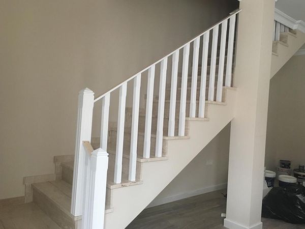 Escalera con barandilla y balaustres blancos, escalones y paredes beige. Bolsas de basura negras y botes de pintura cerca del final.