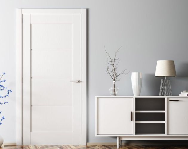 Puerta blanca con paneles de vidrio, junto a un armario blanco con elementos decorativos contra una pared gris.